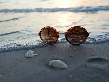 Round sunglasses lie on a sandy beach